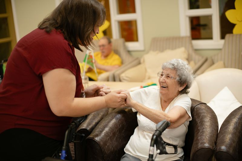 A caregiver holding hands with a smiling older woman in her living room