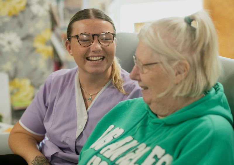 A caregiver and an older woman laughing together at home